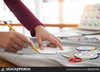 Female fashion designer working with sketches at studio and choosing cloth progress on tailor table