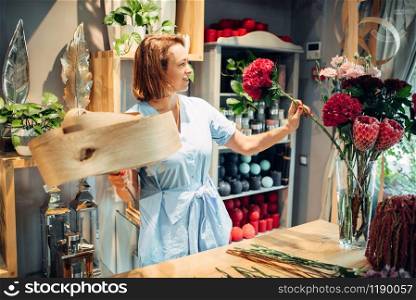 Female florist decorates composition with birch bark on the table in flower shop. Floral artist making bouquet at the workplace. Florist decorates composition with birch bark