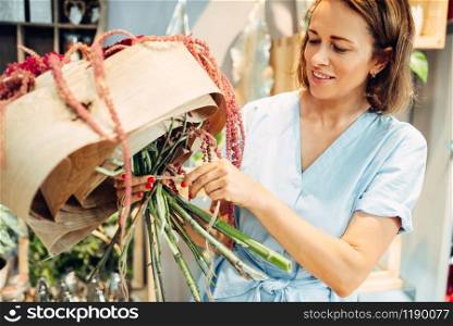 Female florist decorates with bunch flower bouquet in shop closeup. Floral artist making composition at the workplace. Florist decorates flower bouquet in shop closeup