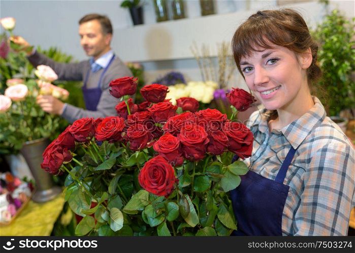 female florist holding glass vase with roses in flower shop