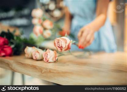 Female florist makes rose composition on the table in flower shop. Floral artist making bouquet at the workplace. Florist makes rose composition in flower shop