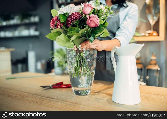 Female florist making flowers arrangement on the table in shop. Floral artist decorates bouquet at the workplace. Florist making flowers arrangement in shop