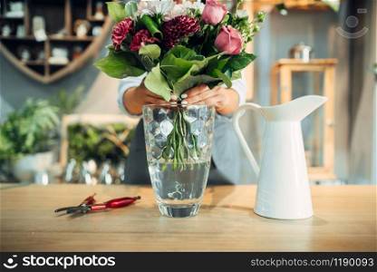 Female florist puts fresh flower bouquet into a vase in floral shop. Floristry service, floristic business