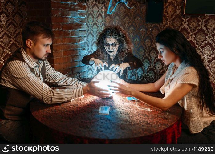 Female foreteller calls the spirits over a crystal ball, witchcraft. Scary witch reads a magic spell, young people hands up on spiritual seance. Foreteller calls the spirits over a crystal ball