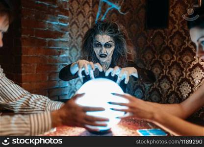 Female foreteller calls the spirits over a crystal ball, witchcraft. Scary witch reads a magic spell, young people hands up on spiritual seance