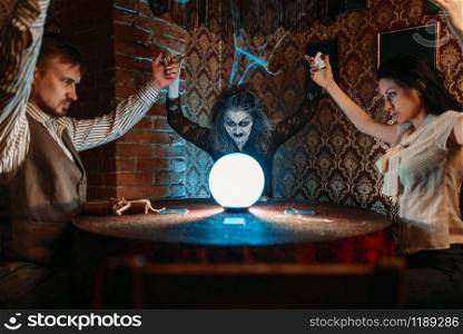 Female foreteller calls the spirits, witchcraft. Scary witch reads a magic spell over a crystal ball, young people hands up on spiritual seance. Female foreteller calls the spirits, witchcraft