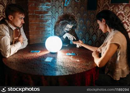 Female foreteller guessing by hand over a crystal ball, witchcraft. Scary witch reads a magic spell, young woman on spiritual seance. Foreteller guessing by hand over a crystal ball