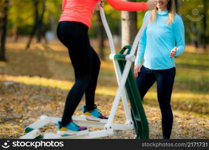 Female Friends Exercising on Outdoor Fitness Equipment in Public Park. Autumn, Fall.. Friends Exercising, Using Outdoor Fitness Equipment in Public Park. Autumn, Fall.