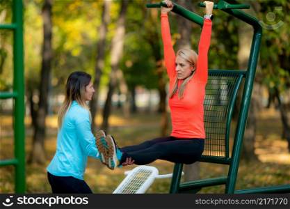 Female Friends Exercising on Outdoor Fitness Equipment in Public Park. Autumn, Fall.. Friends Exercising, Using Outdoor Fitness Equipment in Public Park. Autumn, Fall.