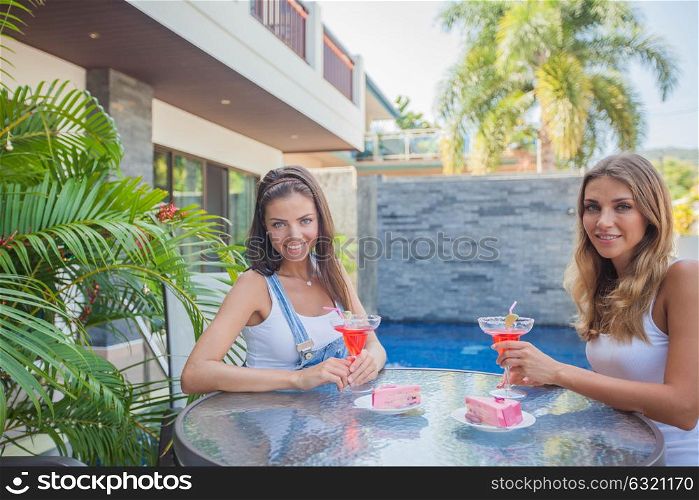 Female friends in outdoor cafe. Female friends sitting in outdoor cafe with cocktail and cake enjoying summer tropical vacation