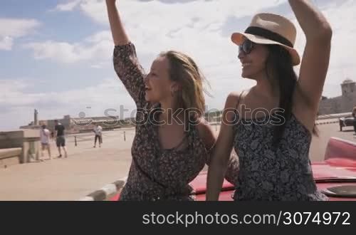 Female friends on holidays, people traveling, young women having fun on vacation, two happy girls smiling in Havana, Cuba. Hispanic persons laughing on old classic convertible car. Slow motion
