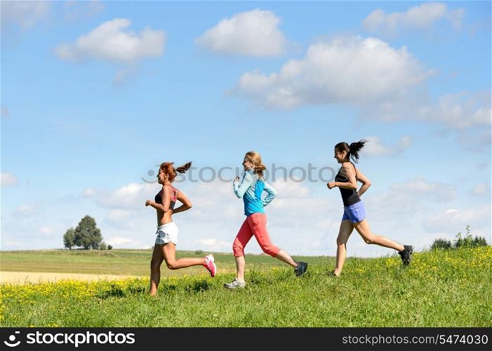 Female friends running downhill through sunny meadow summer sport