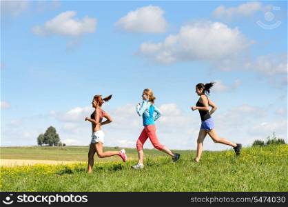 Female friends running downhill through sunny meadow summer sport