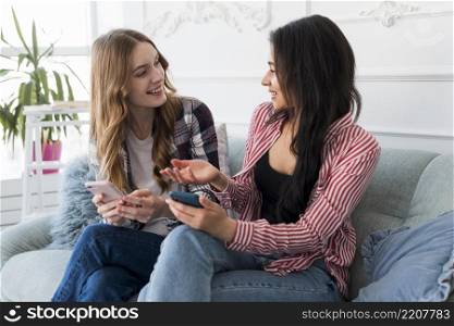 female friends talking while holding smartphones