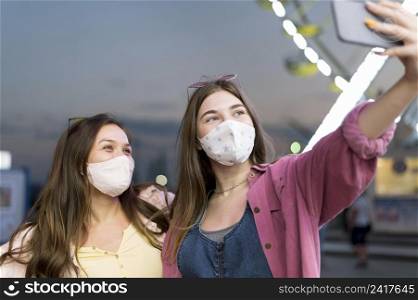 female friends with masks taking selfie amusement park