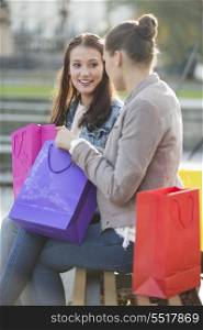 Female friends with shopping bags communicating while sitting on bench