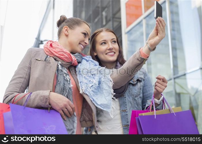 Female friends with shopping bags taking self portrait through mobile phone