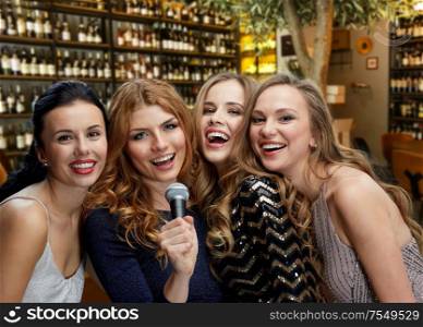 female friendship, leisure and luxury concept - happy women with microphone singing karaoke over restaurant or wine bar background. happy young women with microphone singing karaoke