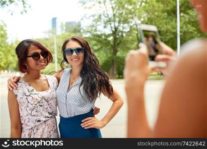 female friendship, technology and people - woman with smartphone photographing her friends in summer park. woman photographing her friends in summer park