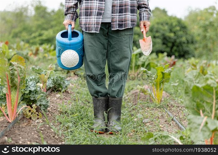 Female gardener concept a gardener holding the blue watering can and metal shovel standing among evergreen vegetable field with a variety of plants.