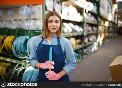Female gardener in apron and gloves in shop for gardening. Woman sells equipment in store for floriculture, florist instrument sale