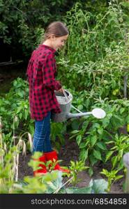 Female gardener watering garden bed with ripe vegetables