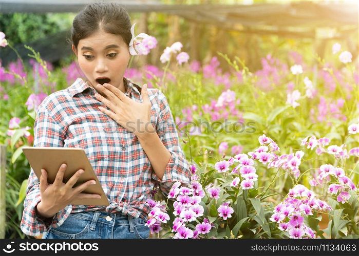Female gardeners wear plaid shirts. There were orchids picking up the ears, Her was surprised when watching tablet and smiling with joy. new generation farmer, gardeners concept.