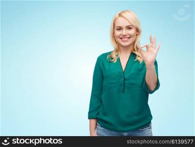 female, gender, gesture, plus size and people concept - smiling young woman in shirt and jeans showing ok hand sign over blue background