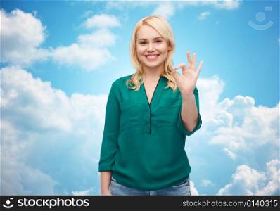female, gender, gesture, plus size and people concept - smiling young woman in shirt and jeans showing ok hand sign over blue sky and clouds background