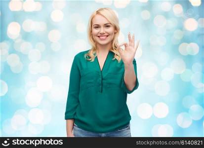 female, gender, gesture, plus size and people concept - smiling young woman in shirt and jeans showing ok hand sign over blue holidays lights background