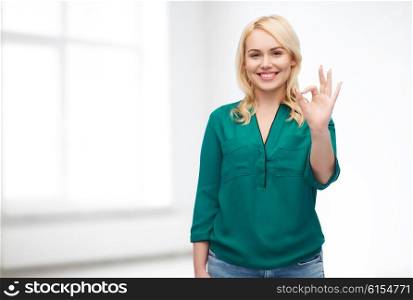 female, gender, gesture, plus size and people concept - smiling young woman in shirt and jeans showing ok hand sign over white room background