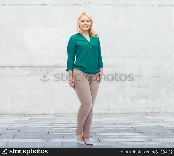 female, gender, portrait, plus size and people concept - smiling young woman in shirt and trousers over urban concrete background