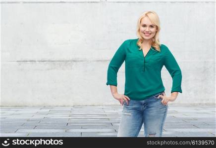 female, gender, portrait, plus size and people concept - smiling young woman in shirt and jeans over gray concrete wall background