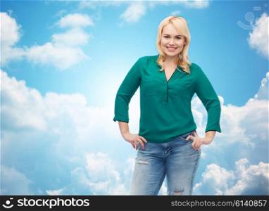 female, gender, portrait, plus size and people concept - smiling young woman in shirt and jeans over blue sky and clouds background