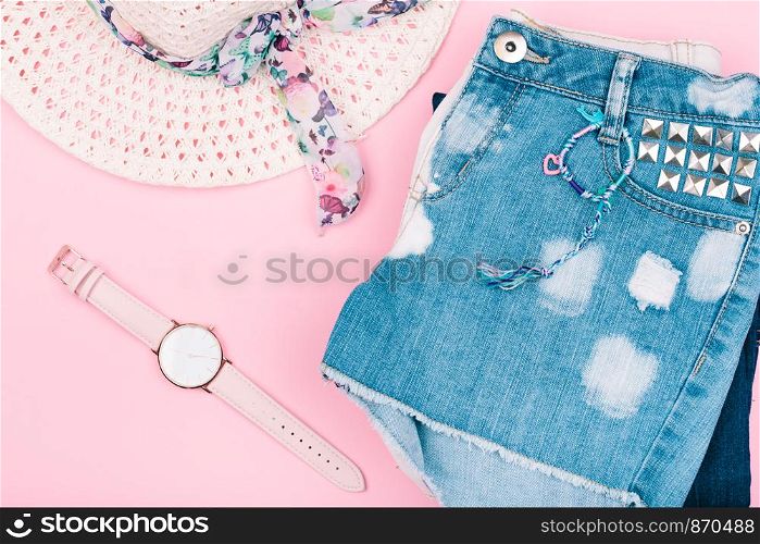 Female girlish clothes, blue jeans shorts, hat, watch on pink background