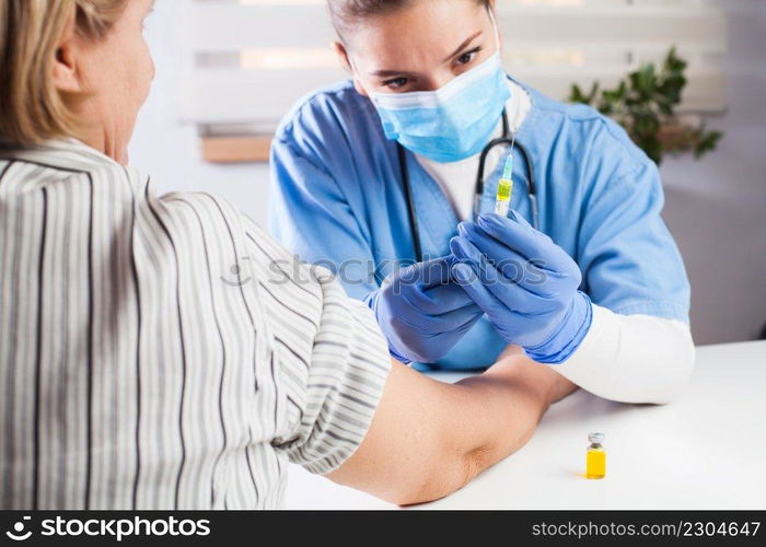 Female GP doctor holding&oule vial yellow liquid,filling syringe jab with injection shot,vaccinating elderly patient,Coronavirus COVID-19 virus disease immunization concept,vaccine clinical trial