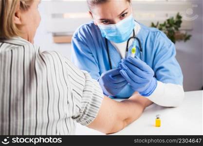 Female GP doctor holding&oule vial yellow liquid,filling syringe jab with injection shot,vaccinating elderly patient,Coronavirus COVID-19 virus disease immunization concept,vaccine clinical trial