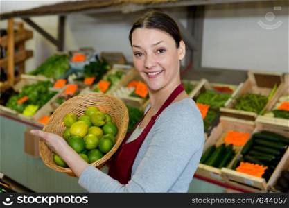 female greengrocer holding basket of limes