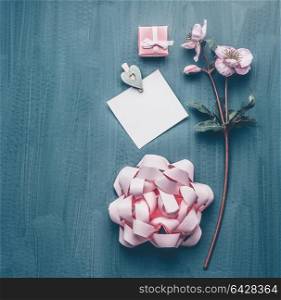 Female greeting background with decorative flowers, bow, pink gift box and card mock up, top view. Women&rsquo;s Day or Mother&rsquo;s Day layout concept
