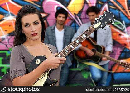 Female guitarist standing with band members in front of a graffitied wall