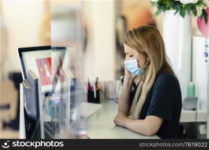 Female hairdresser answering the phone to give her clients an appointment, wearing a protective mask, at a hairdresser&rsquo;s. Business and beauty concepts. Female hairdresser answering the phone to give her clients an appointment, wearing a protective mask