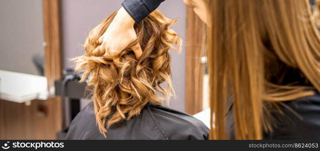 Female hairdresser checks brown curly hairstyle of a young caucasian woman in beauty salon. Female hairdresser checks brown curly hairstyle of a young caucasian woman in beauty salon.