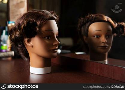 Female hairdressing mannequin is located on a wooden table, hairdressing tools on the background.. Hairdressing mannequin located on a wooden table.