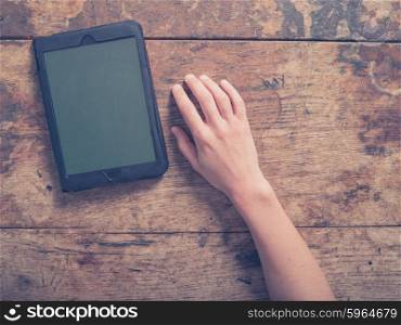 Female hand and a tablet computer on a wooden table