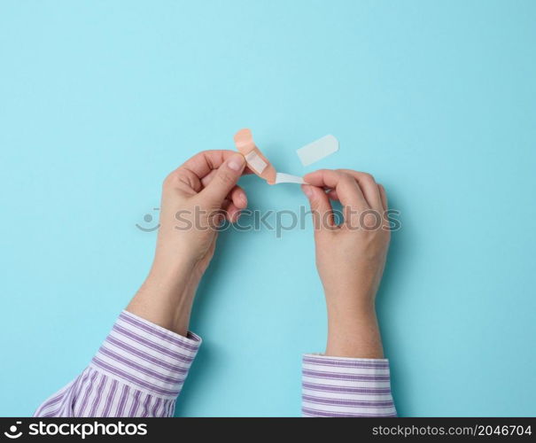 female hand and brown medical adhesive plaster for the treatment of injuries and cuts on the skin, blue background