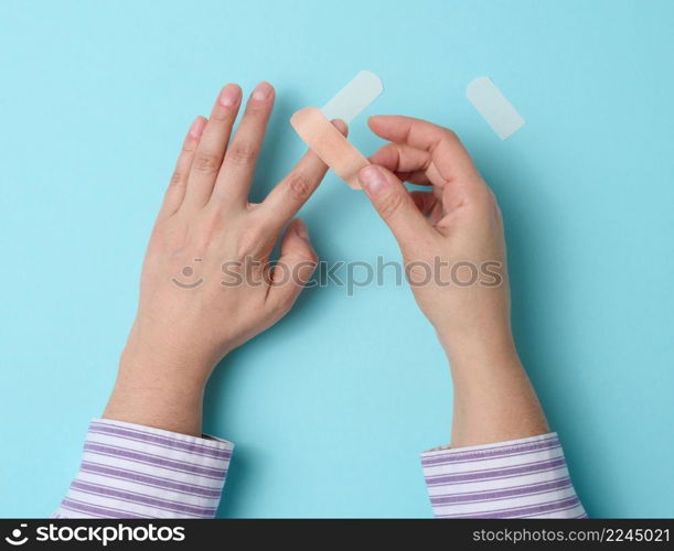 female hand and brown medical adhesive plaster for the treatment of injuries and cuts on the skin, blue background