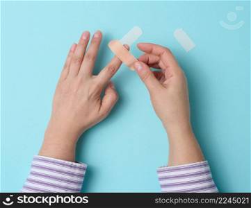 female hand and brown medical adhesive plaster for the treatment of injuries and cuts on the skin, blue background