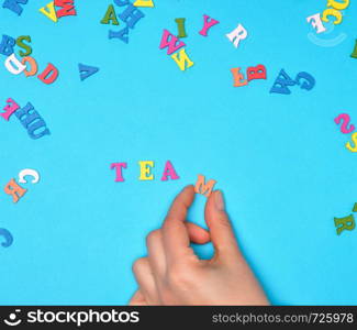 female hand and multicolored wooden letters of the English alphabet on a blue background, inscription team