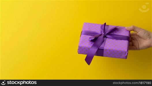 female hand are holding a purple gift box on a yellow background, happy birthday concept