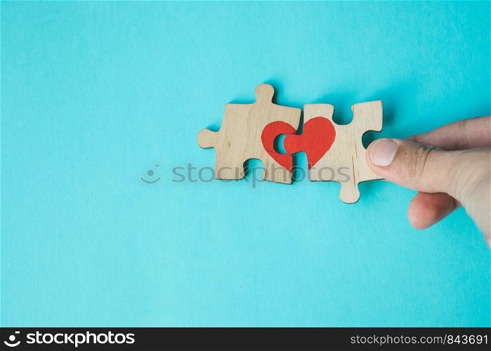 Female hand connecting puzzle with drawn red heart on blue background. Love concept. St. Valentine day. Reconciliation. Reunion concept. Free space for text. Female hand connecting puzzle with drawn red heart on blue background. Love concept. St. Valentine day. Reconciliation. Reunion concept. Copy space.